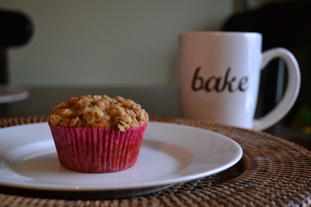 Soft oatmeal snack muffin in pink liner on white plate with coffee mug labeled "bake" in background, perfect for baking lovers.