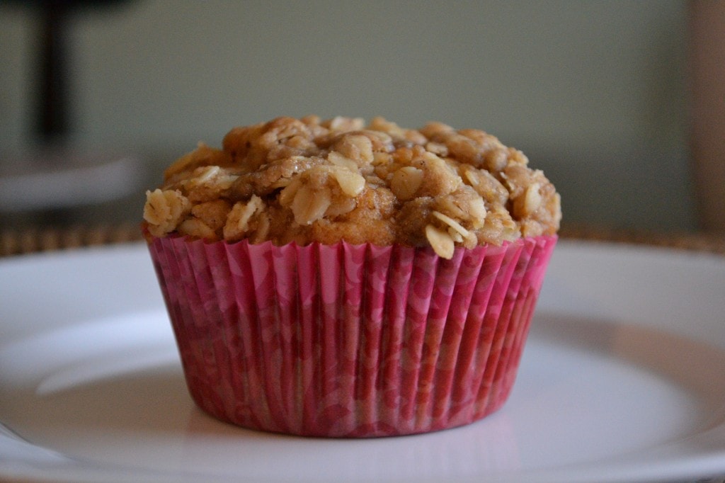 Crunchy oatmeal muffin with chopped nuts in a pink cupcake liner on a white plate.