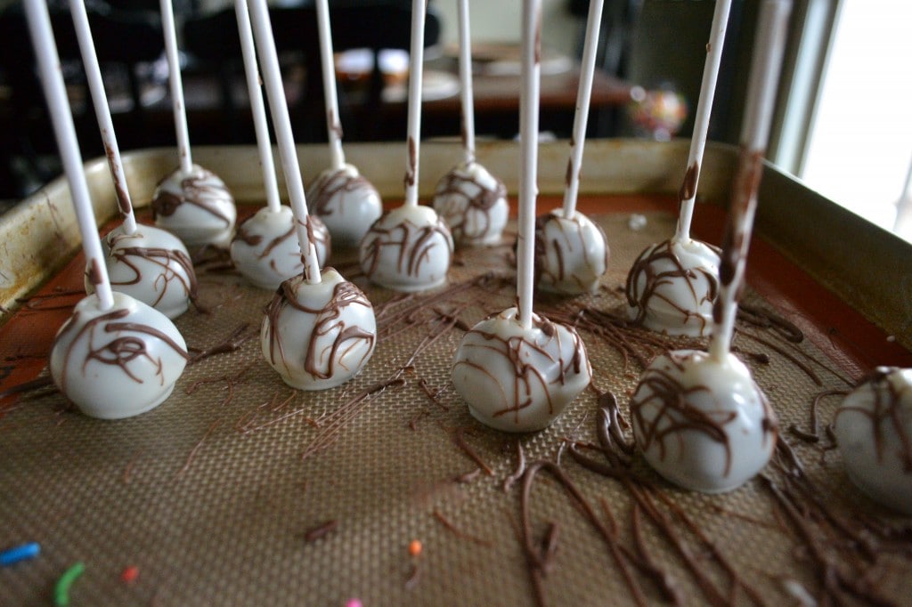 Chocolate-covered cake pops decorated with white coating and drizzle, arranged on a baking sheet ready for presentation or serving.