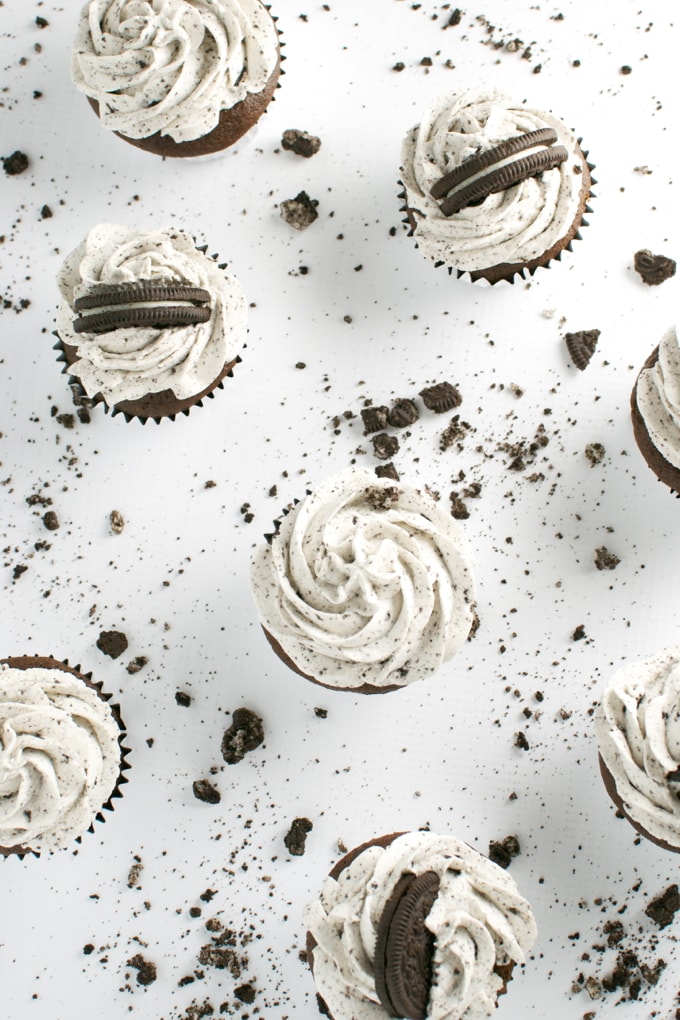 Cream-filled chocolate cupcake with Oreo cookie topping and cookie crumbs, on white background.
