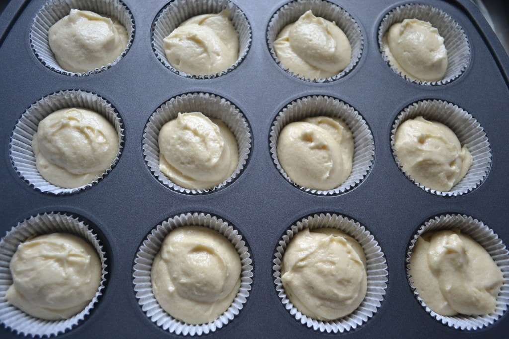 Cream-colored batter in cupcake liners inside a muffin tray, ready for baking, showcasing homemade cupcake preparation in a kitchen setting.