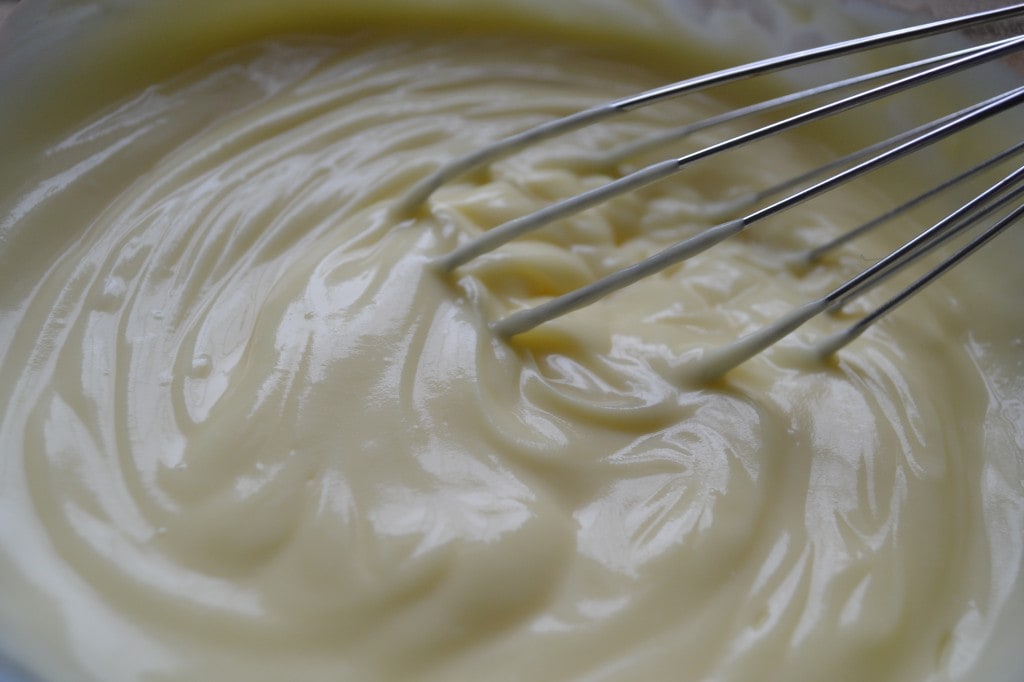 Creamy vanilla frosting being mixed with a whisk in a bowl.