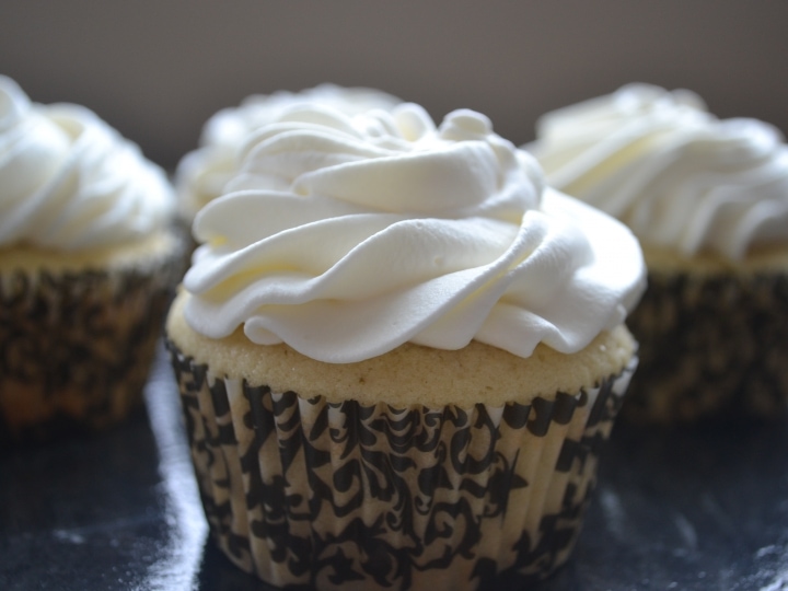 Delicious vanilla cupcake with whipped white frosting, topped with elegant swirls, baked fresh with chocolate and vanilla cupcake liners, perfect for sweet treats or celebrations.