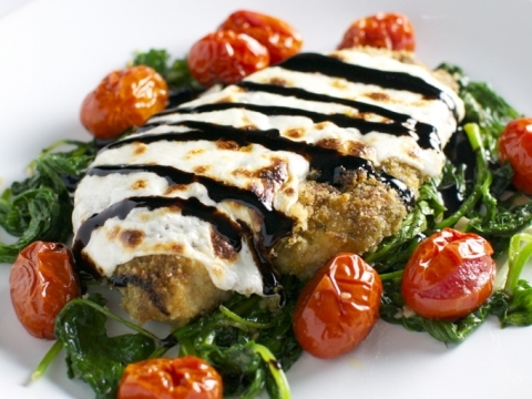 Grilled chicken Parmesan with melted cheese and balsamic glaze on bed of sautéed greens and cherry tomatoes. A delicious and flavorful Italian-inspired dish perfect for dinner.