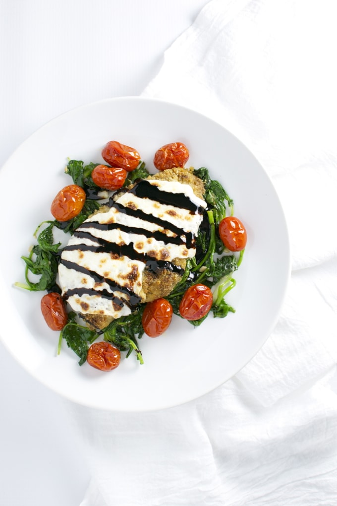 Golden-crusted chicken topped with creamy sauce and balsamic glaze, served over sautéed greens with cherry tomatoes for a healthy, flavorful meal.