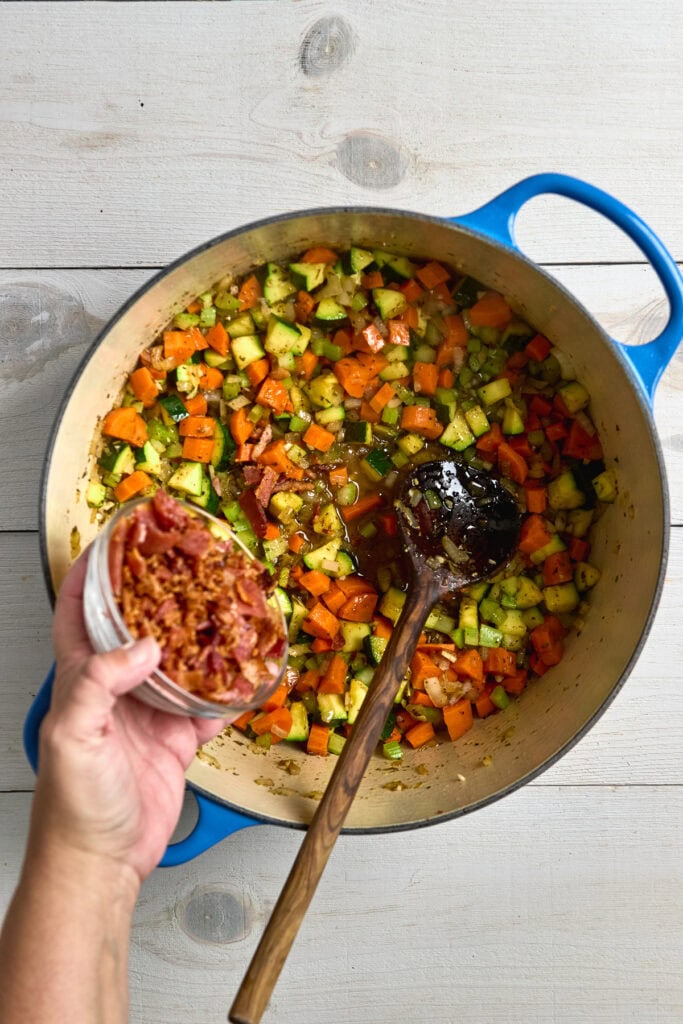Colorful sautéed mixed vegetables with bacon bits in a large pot, ready for cooking or recipe preparation.