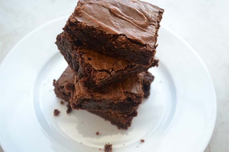 Rich, decadent chocolate brownies stacked on a white plate, showcasing their fudgy texture and glossy chocolate topping, perfect for sweet indulgence.