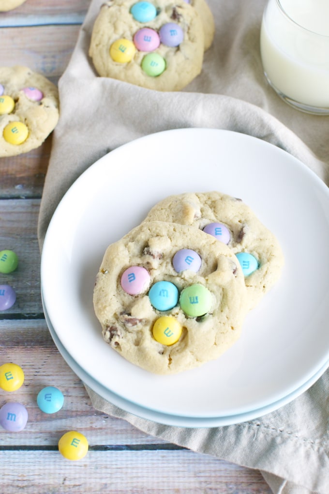 Colorful Easter M&M cookies on white plate with milk, tasty treat, festive dessert, colorful candies, homemade cookies, sweet snack, celebration dessert, Easter sweets, baking, chewy cookies.