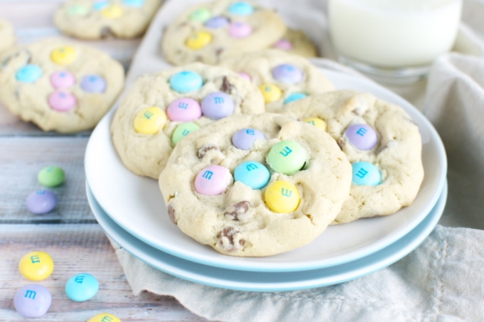 Colorful M&M cookies with rainbow candy toppings on a white plate, perfect for sweet snack cravings. Enjoy soft, chewy cookies filled with chocolate and vibrant M&Ms for a fun treat.