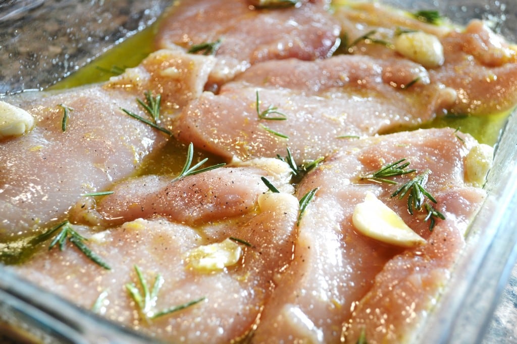 Juicy raw chicken breasts seasoned with garlic and rosemary in a glass baking dish. Perfect for marinating or baking delicious, flavorful chicken dishes.