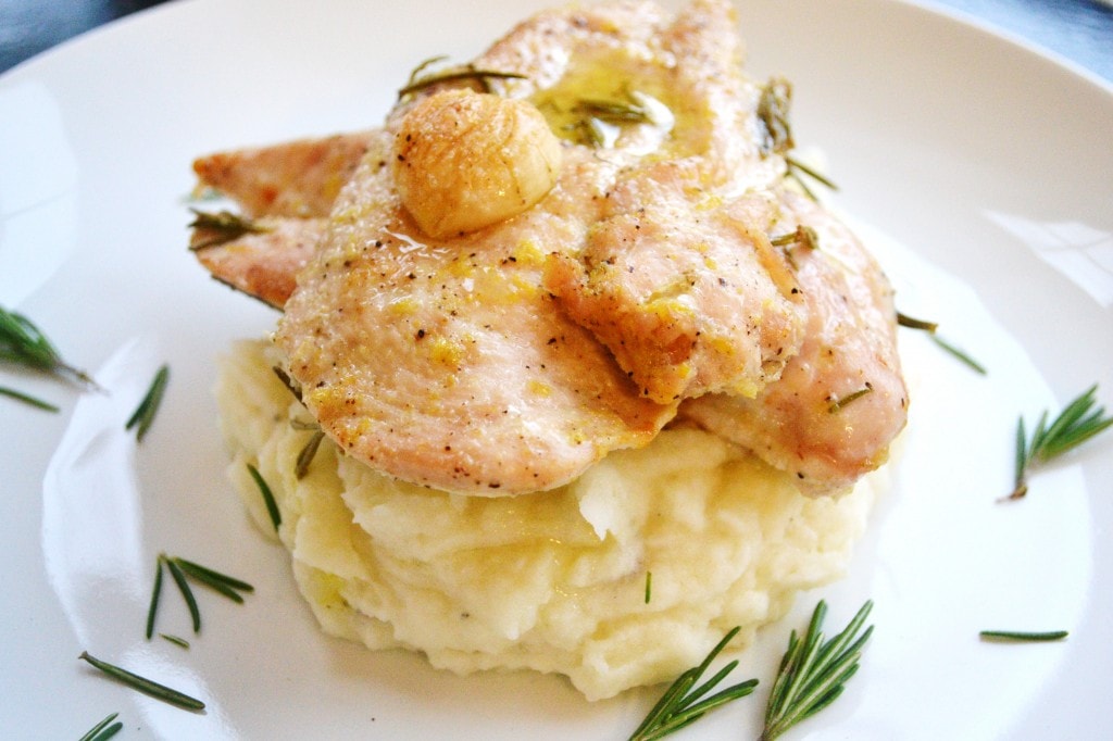 Creamy chicken over mashed potatoes garnished with rosemary and garlic. Perfect comfort food dish served on a white plate, showcasing fluffy mashed potatoes topped with seasoned chicken.