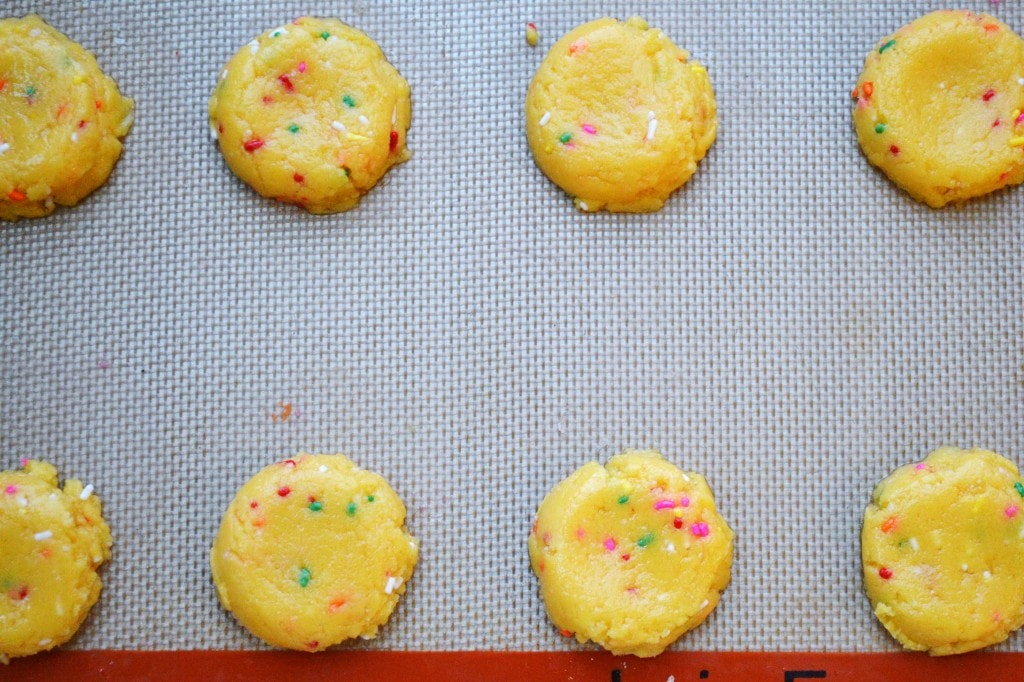Colorful sprinkle-coated cookie dough balls on baking sheet for festive treats, perfect for baking or snacking.