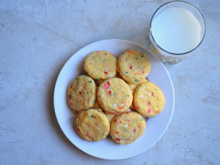 Colorful confetti sprinkle cookies with a glass of milk on a white plate, perfect for sweet treats and dessert recipes.