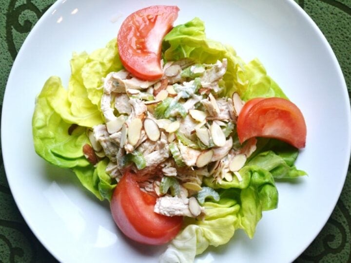 Fresh chicken salad served on a bed of lettuce with tomato slices, topped with sliced almonds, ideal for healthy eating and meal prep.