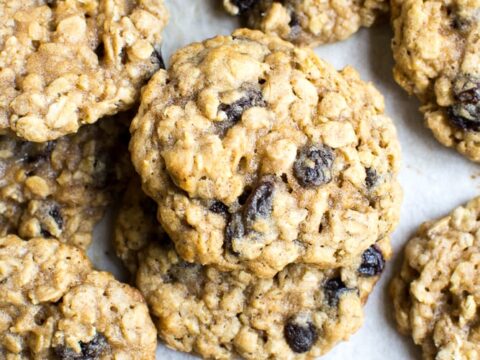 Chewy oatmeal raisin cookies with oats and dried fruit on parchment paper, featuring a golden-brown, crunchy exterior and soft interior. Perfect for snacking or dessert.