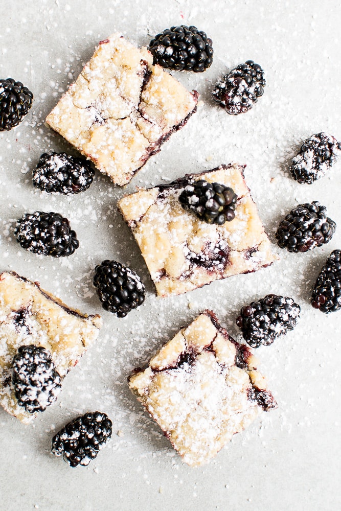 Blackberry Blondie Bars with Powdered Sugar Dusting, Fresh Blackberries, and Flaky Pastry on Light Background, Easy Blackberry Dessert Recipe, Unique Blackberries and Blondies Recipe, Blackberry Pastry Dessert, Sweet Blackberries and Crispy Blondie Bars.