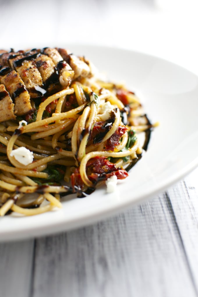 Grilled chicken pasta with sun-dried tomatoes, basil, and balsamic glaze on a white plate.
