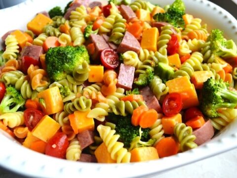 Bright vegetable pasta salad with cherry tomatoes, broccoli, and shredded cheese in a white bowl, perfect for healthy, delicious meals and meal prep.