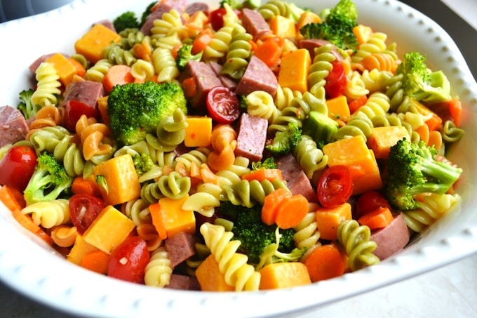 Bright vegetable pasta salad with cherry tomatoes, broccoli, and shredded cheese in a white bowl, perfect for healthy, delicious meals and meal prep.