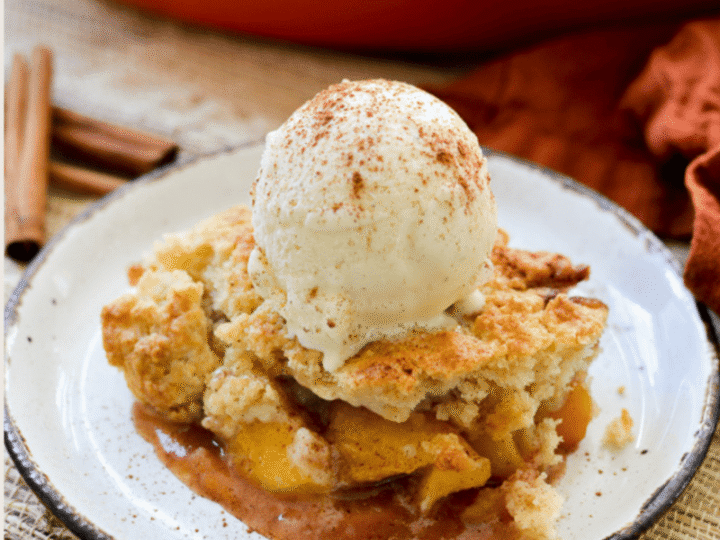 Peach cobbler with vanilla ice cream and cinnamon on top served on a rustic plate.