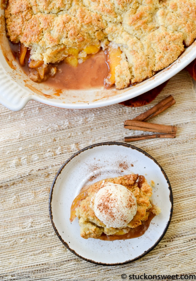 Butterscotch peach cobbler with vanilla ice cream and cinnamon on top, serving as a delicious dessert from Stuck On Sweet. Perfect for fall or anytime sweet cravings hit.