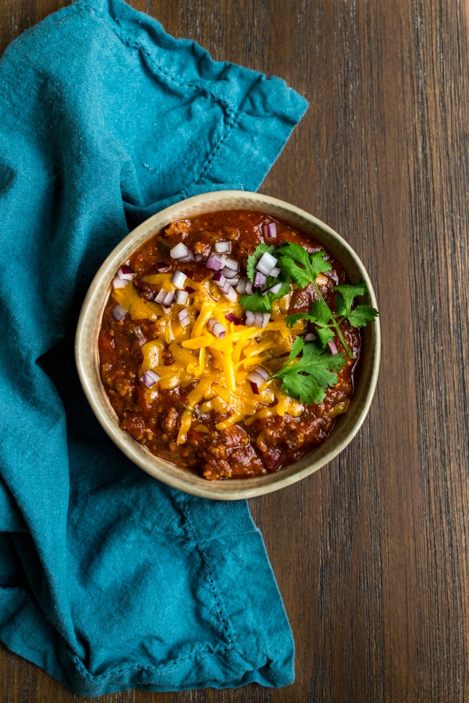 Homemade chili in a bowl garnished with cheese, red onion and cilantro.