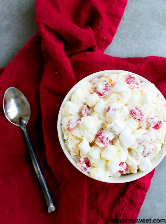 Creamy fruit fluff salad with marshmallows, cherries, and whipped cream in a white bowl on red napkin. Perfect sweet dessert for holidays and gatherings.