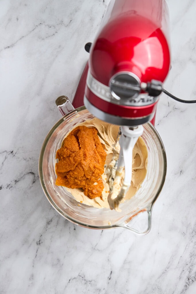 Creamy peanut butter and sweet pumpkin puree in a glass mixing bowl with a red stand mixer for fall dessert recipes.