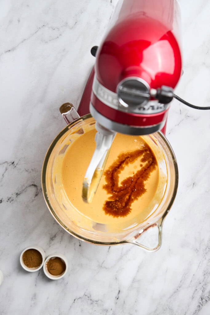 Creamy caramel sauce being mixed with a stand mixer on a marble countertop with cinnamon.