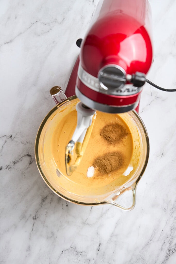 Cream-colored cake batter with cinnamon in a glass mixing bowl and a red stand mixer.