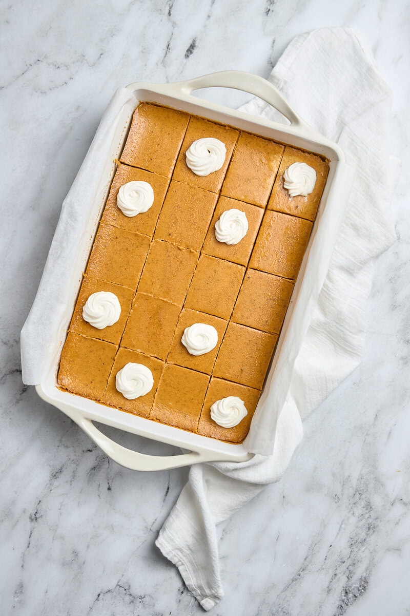 Creamy caramel blondies with dollops of whipped cream in a white baking dish for easy serving. Perfect for sweet snacks, dessert recipes, and holiday gatherings.