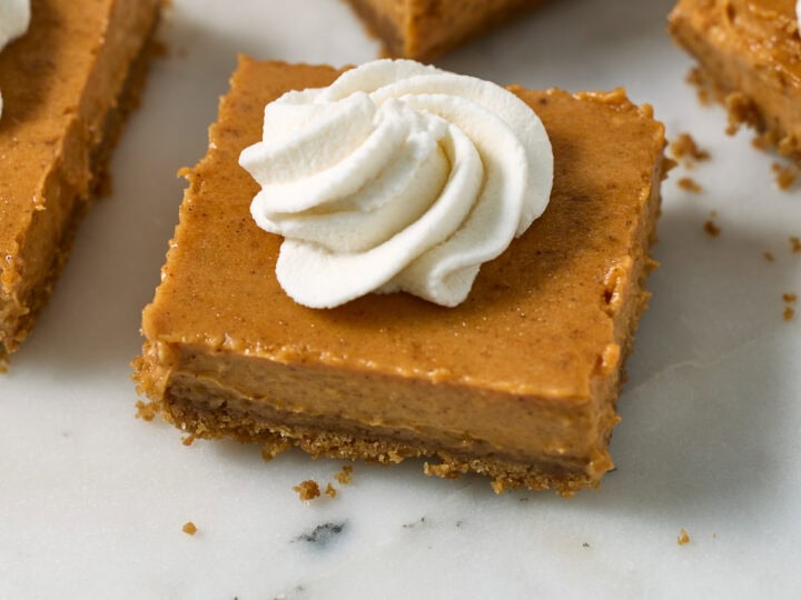 Cream cheese pumpkin bars topped with whipped cream on a white marble serving platter.