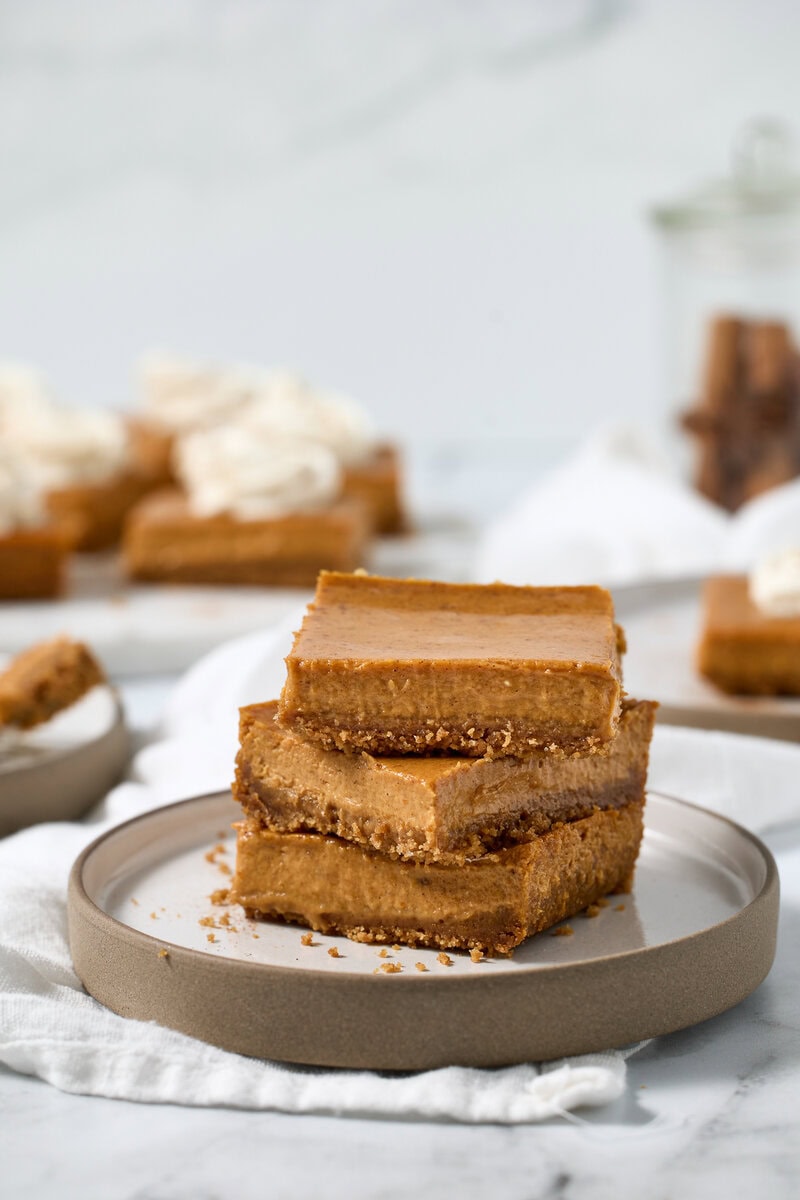Butterscotch candy bars, stacked on a plate, close-up, with blurred background of other caramel treats and whipped cream, showcasing homemade caramel flavor and rich, chewy texture.
