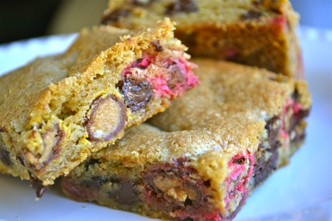 Chewy pink and chocolate chip cookie bars with nuts on white plate.