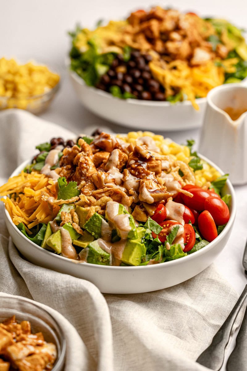 Fresh taco salad bowl with seasoned chicken, diced avocado, cherry tomatoes, shredded cheese, and creamy dressing on a white ceramic dish. Delicious and healthy meal option from Stuck On Sweet.