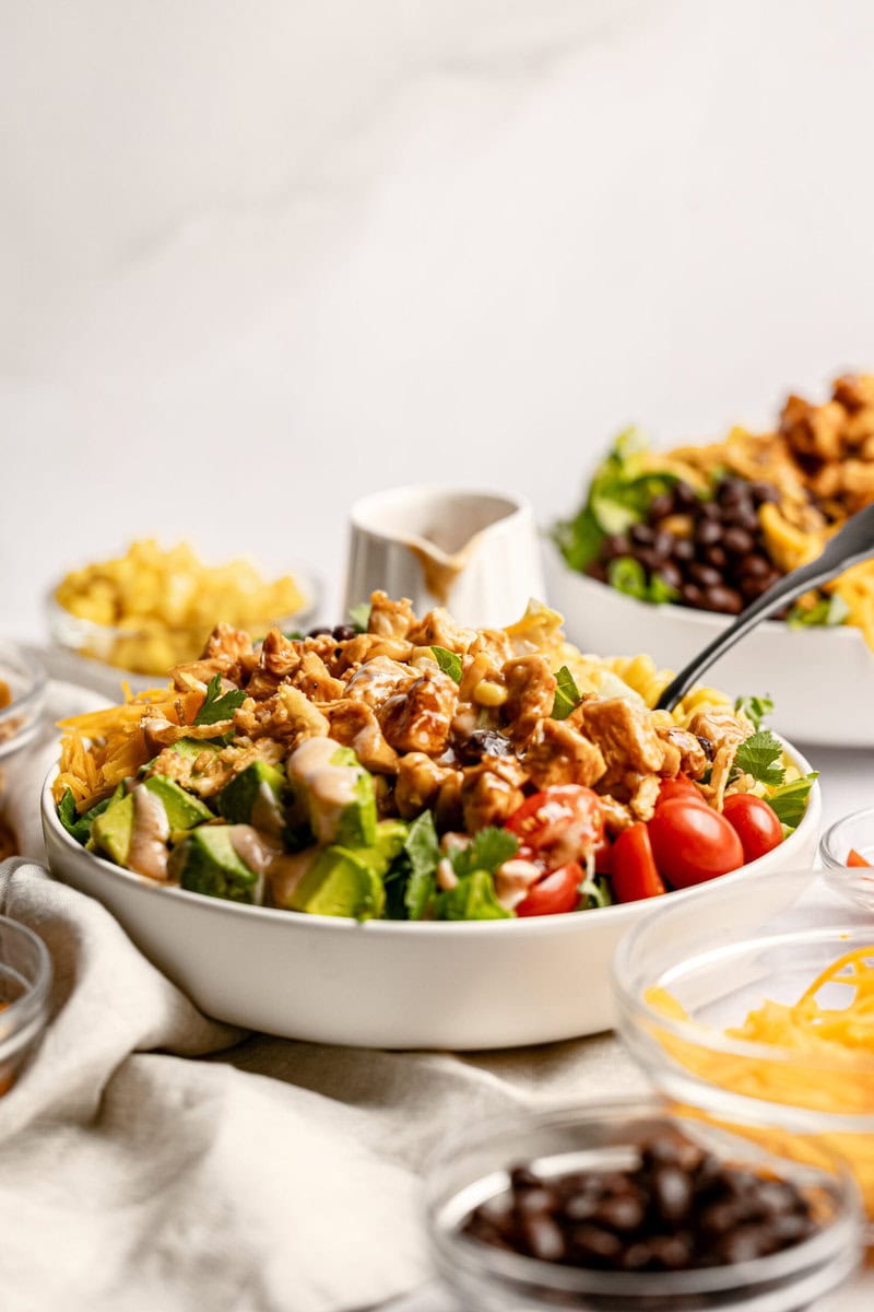 Crispy chicken taco salad with fresh tomatoes and greens, served on a white platter, perfect for Tex-Mex and southwestern cuisine, topped with creamy dressing and colorful toppings.