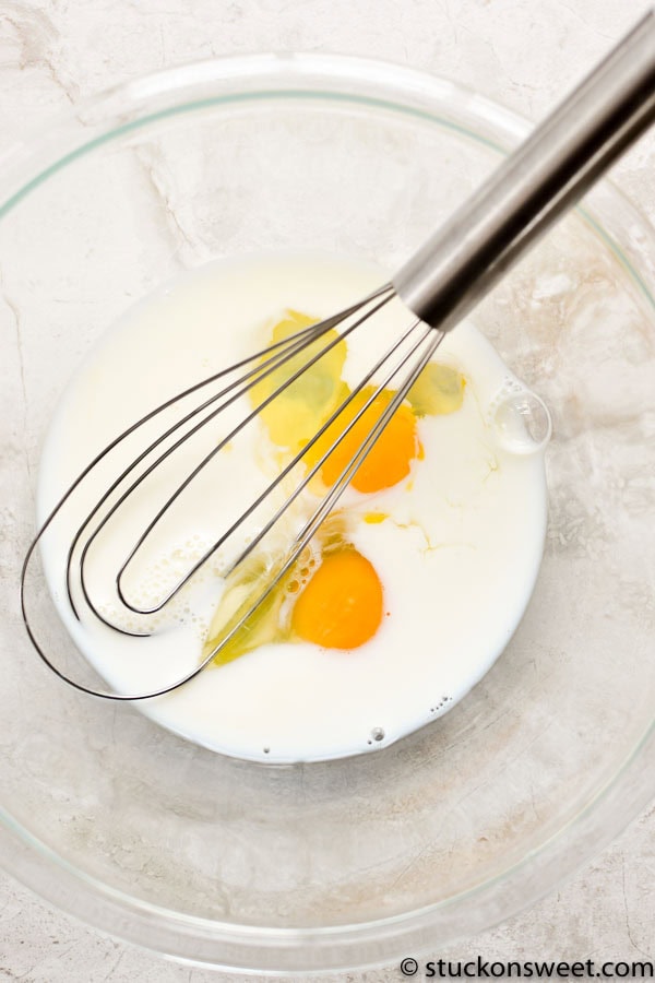 Creamy mixture of eggs and milk for baking or cooking, whisked together in a glass bowl with a metal whisk, ready for a delicious recipe.