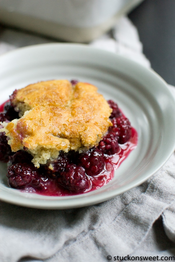 Golden blackberry cobbler with a crispy topping served in a white bowl, featuring fresh berries and a buttery crust, ideal for summer desserts and sweet gatherings.