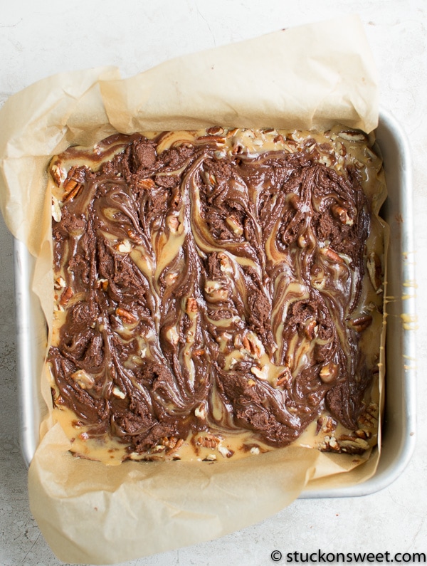 Rich chocolate brownie batter with swirls of caramel and nuts before baking, in a baking dish for indulgent dessert, perfect for chocolate lovers.