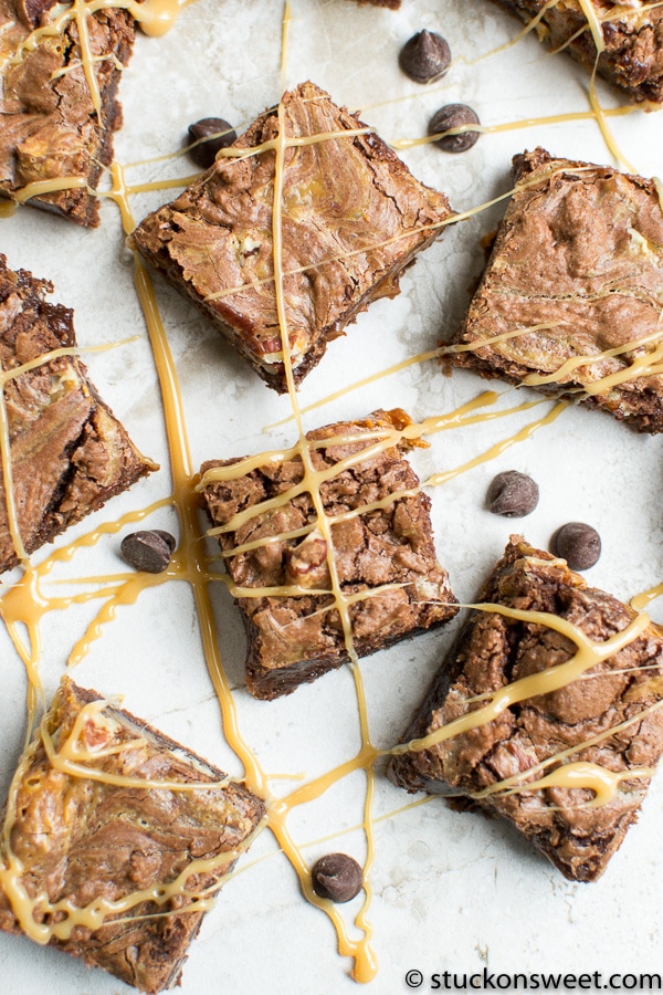 Fudgy brownie bars topped with caramel drizzle and chocolate chips, served on parchment paper. Perfect decadent dessert from Stuck On Sweet for chocolate lovers.