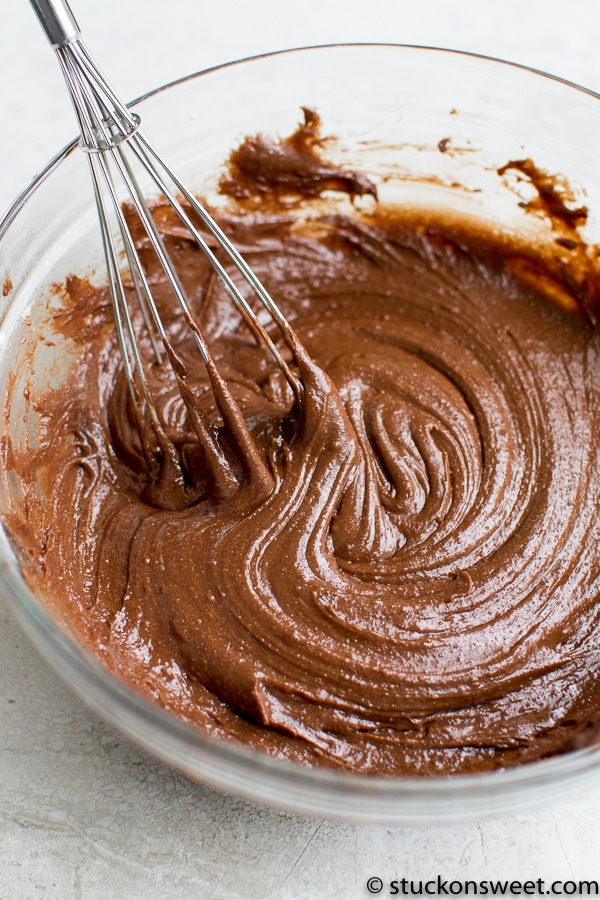 Creamy chocolate frosting in a glass bowl with a whisk attachment mixing the rich, smooth texture for perfect desserts. Ideal for cakes, cupcakes, or cookies.