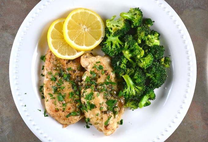 Grilled chicken with lemon slices and steamed broccoli on a white plate, healthy meal with fresh ingredients.