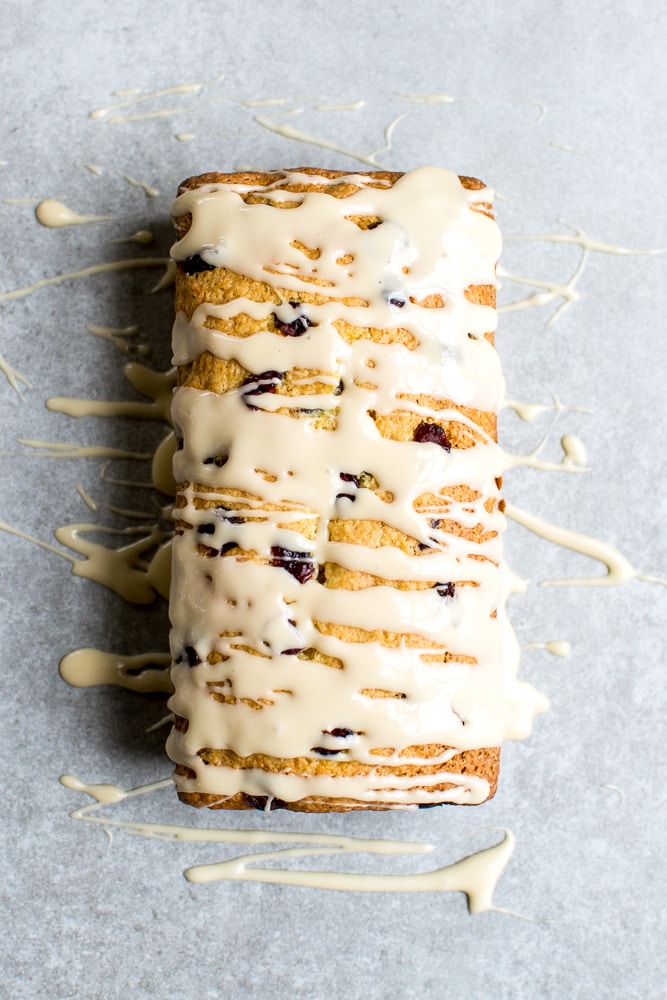 Cream cheese glazed blueberry lemon pound cake with zest and berries on textured gray background.