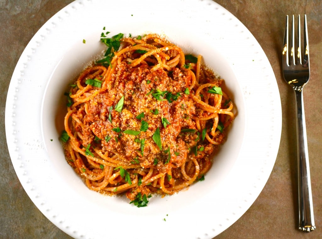 Spaghetti with meat sauce garnish, served on a white plate with parsley and a fork, close-up of classic Italian pasta dish.