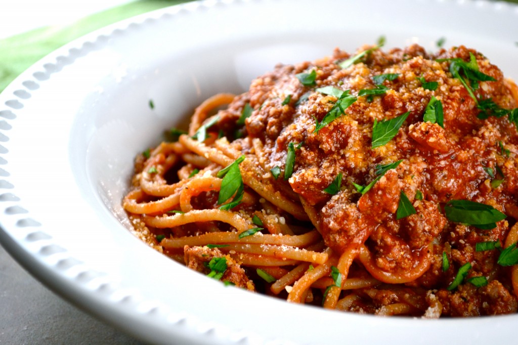 Savory spaghetti with meat sauce garnished with fresh parsley in a white bowl.