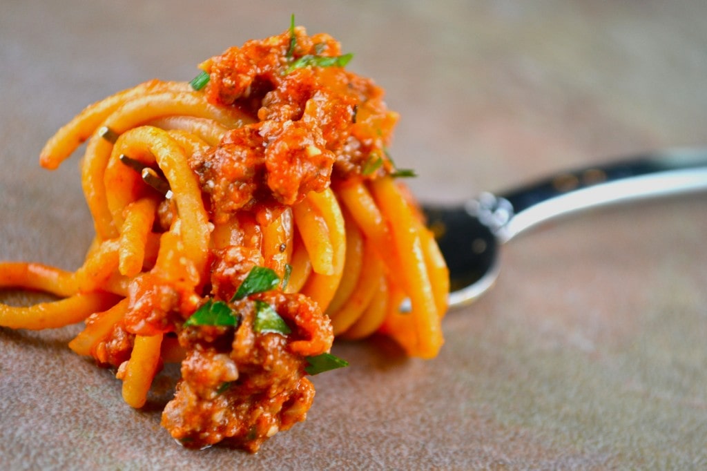 Rich spaghetti with meat sauce garnished with fresh herbs on fork, close-up image of Italian pasta dish.