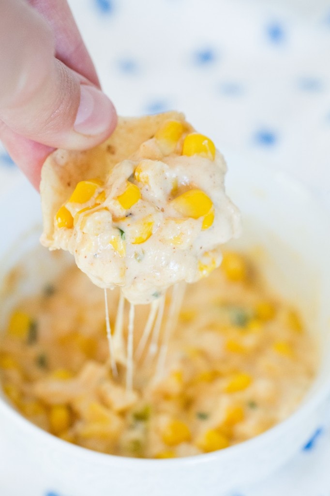 Creamy corn dip with melted cheese and sweet corn kernels, served with a crispy chip.