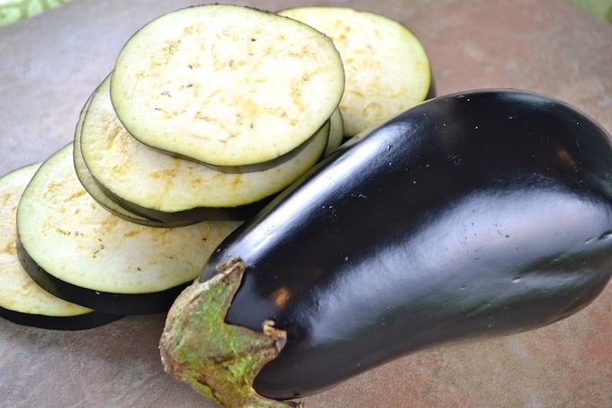 Eggplant slices next to a whole eggplant on a kitchen surface.