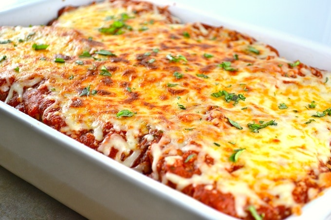 Cheesy baked lasagna in a white baking dish topped with melted cheese and fresh herbs, showcasing a delicious homemade Italian pasta dish.