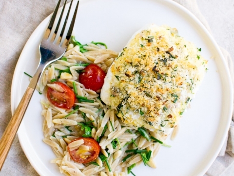 Baked cod fish with crispy crust served with pasta salad and cherry tomatoes on a white plate. Perfect for healthy dinner or seafood lovers.